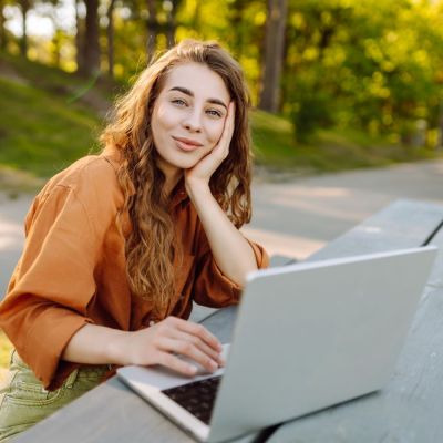 Entspannt blickende Frau auf einer Bank vor ihrem Notebook